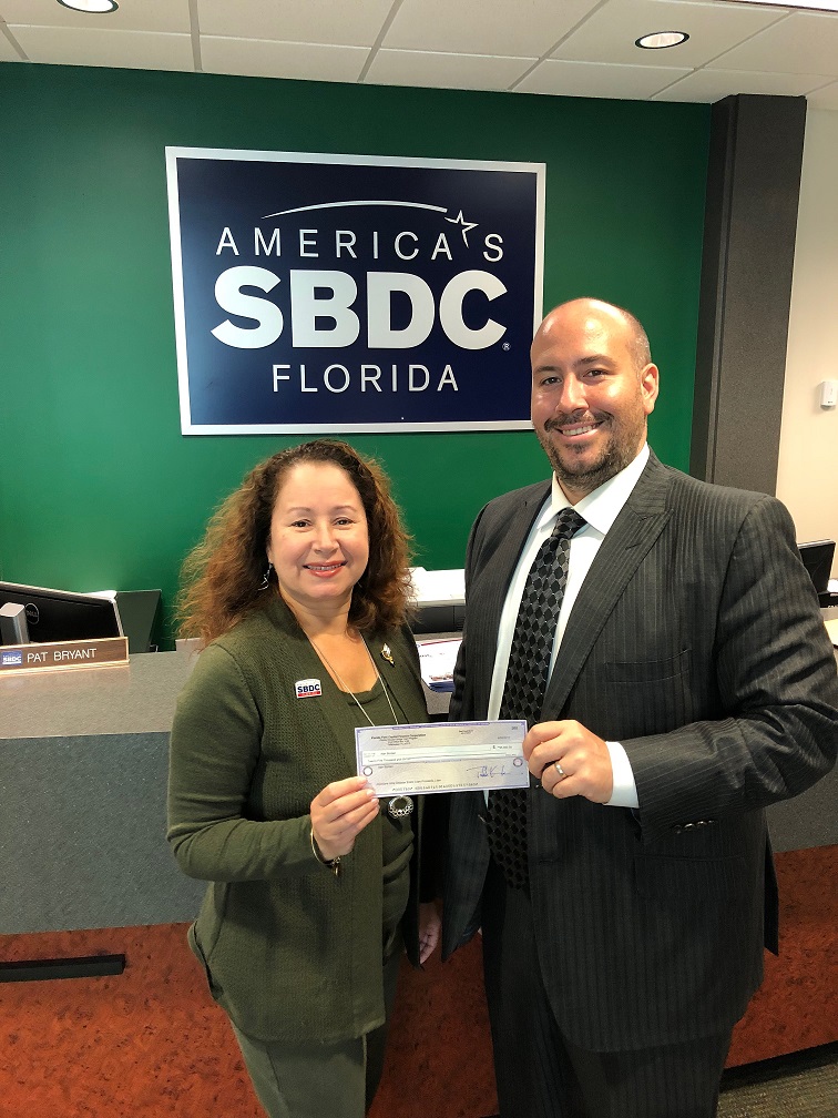 Alan Borden, owner of Debt Relief Legal Group, accepts an emergency bridge loan check from Eileen Rodriguez, Regional Director of the Florida SBDC at USF