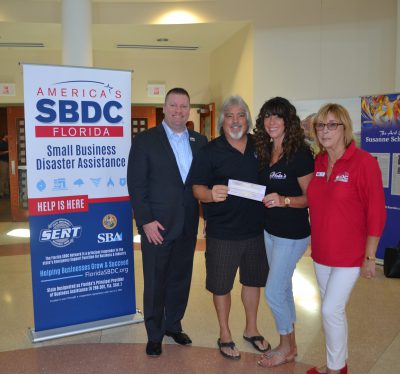 Mike Myhre, CEO of the Florida SBDC Network, presents the Viola's with a check for their Florida Small Business Emergency Bridge Loan following Hurricane Irma