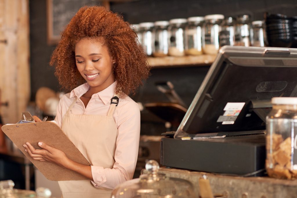 minority-owned business woman behind counter holding clipboard 