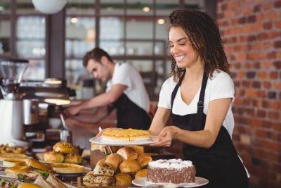 Smiling waitress holding cake in front of colleague at coffee shop